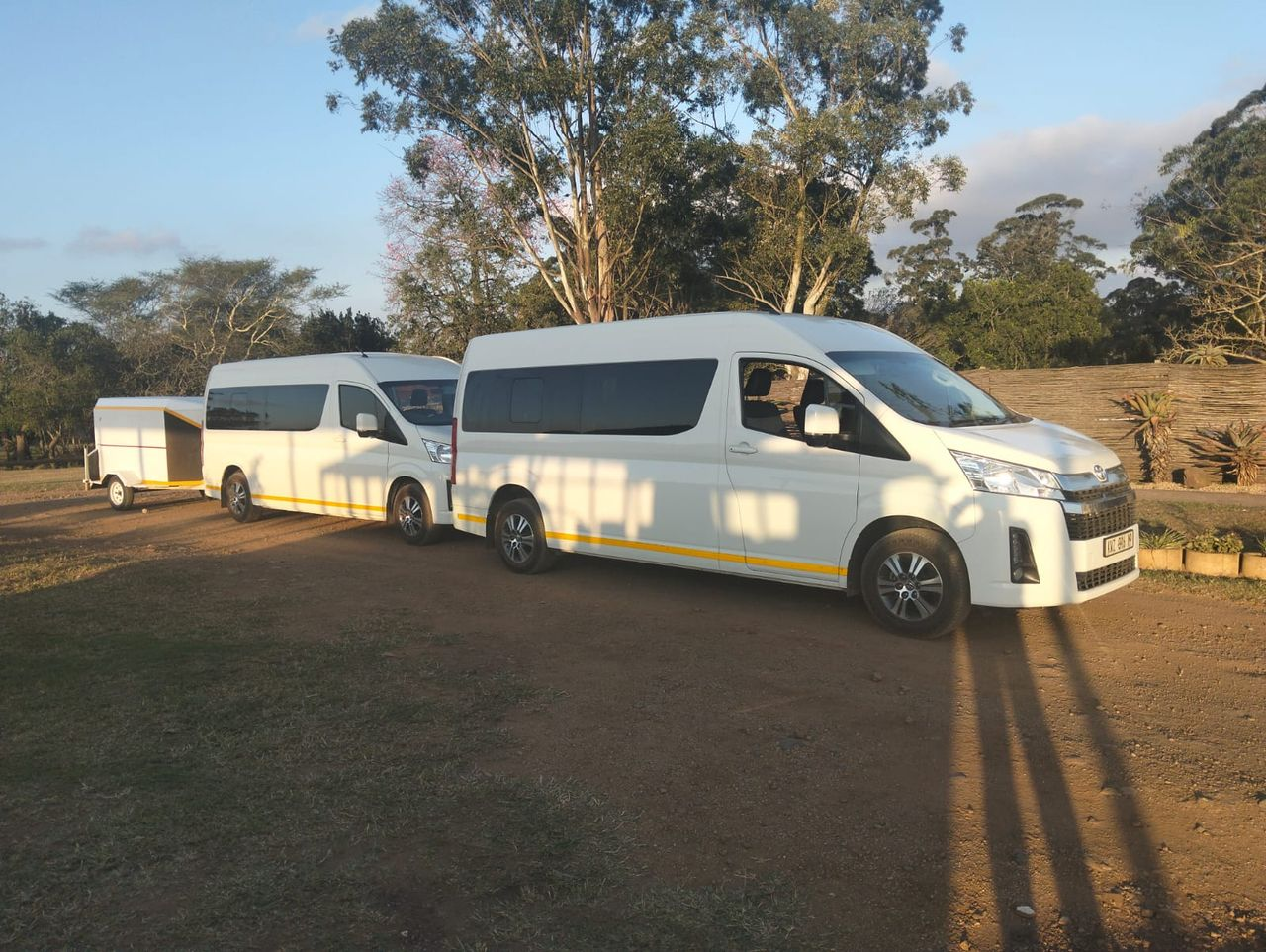 Two Toyota Hiace shuttles and a luggage trailer at golden hour