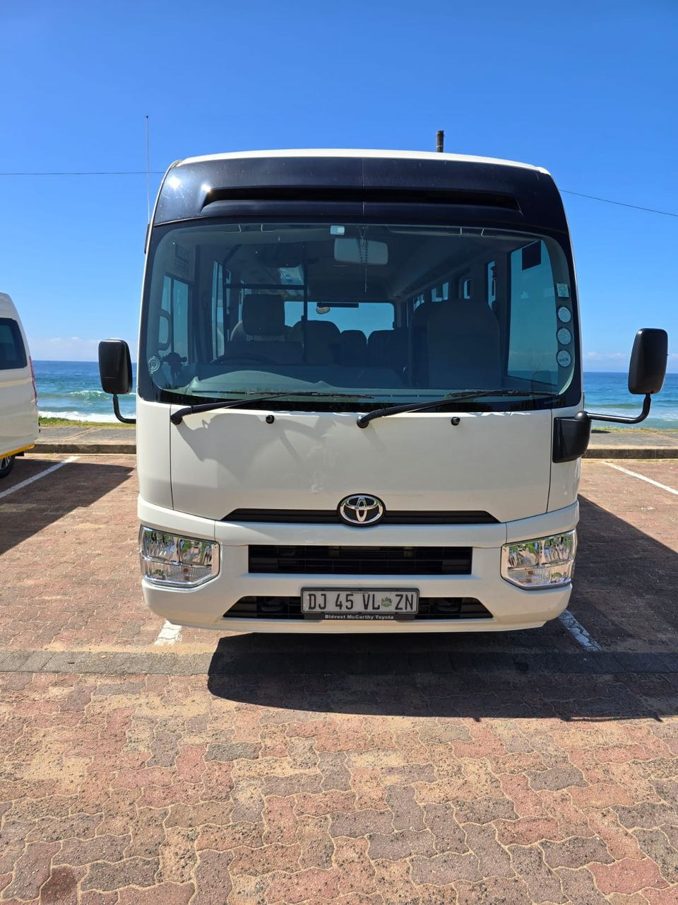 Front view of the Toyota Coaster tour bus beside the Indian Ocean