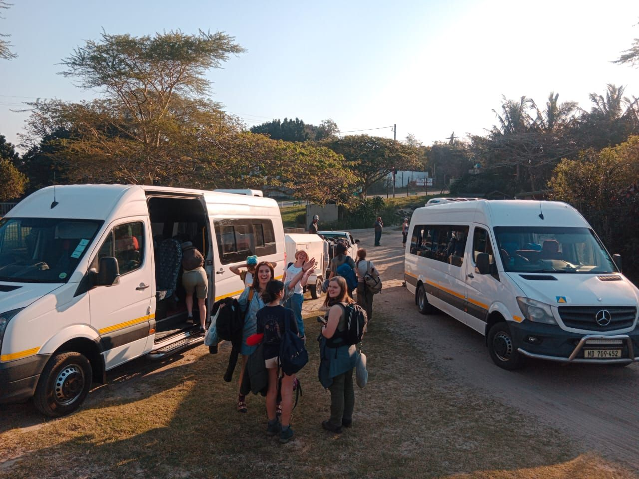 Tour group boarding Mercedes-Benz Sprinter shuttles at golden hour